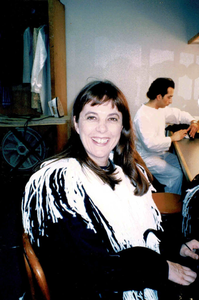 Sue sitting in the dressing room, wearing the Fly costume (minus the head) and smiling at the camera.