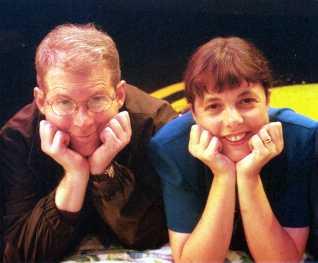A man and a woman with their head in their hands, smiling a the camera.