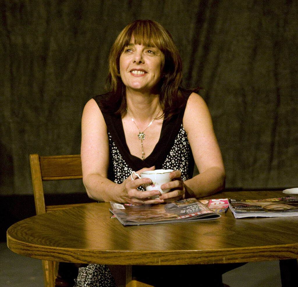 Playing Anita sitting at a table.